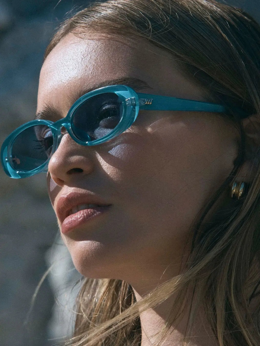 A close-up profile shot of a woman looking upward while wearing the translucent teal Le Specs Sunglasses Outta Love + in Blue Pearl | Twentyseven Toronto