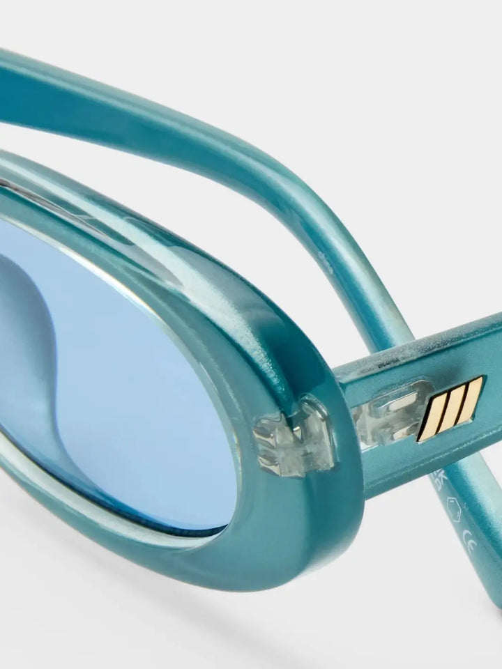 A detailed macro shot focusing on the hinge mechanism and gold logo detail of the Le Specs Sunglasses Outta Love + in Blue Pearl frames | Twentyseven Toronto