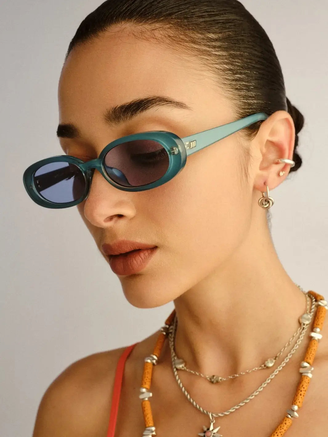 A close-up portrait of a woman looking downward, showcasing the side profile and tinted lenses of the Le Specs Sunglasses Outta Love + in Blue Pearl | Twentyseven Toronto