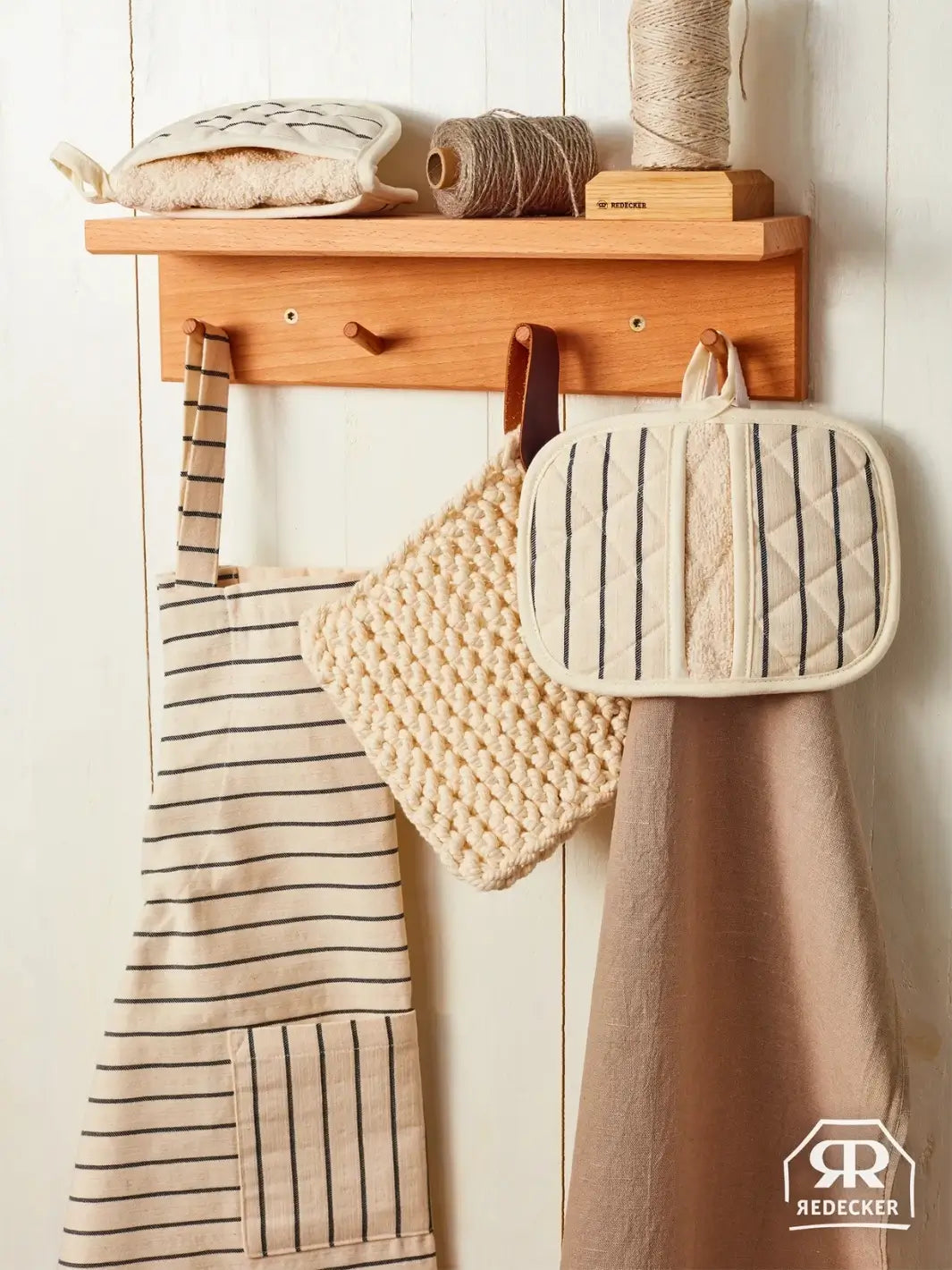 Wooden wall shelf with kitchen towels and potholders hanging on hooks from Burstenhaus Redecker against a white wall | Twentyseven Toronto