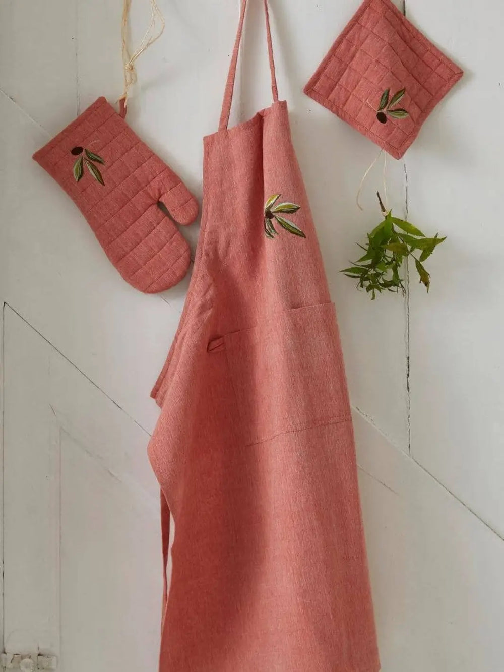 Red apron with matching oven mitts and pot holders from Sylvie Thiriez on a white wooden background | Twentyseven Toronto