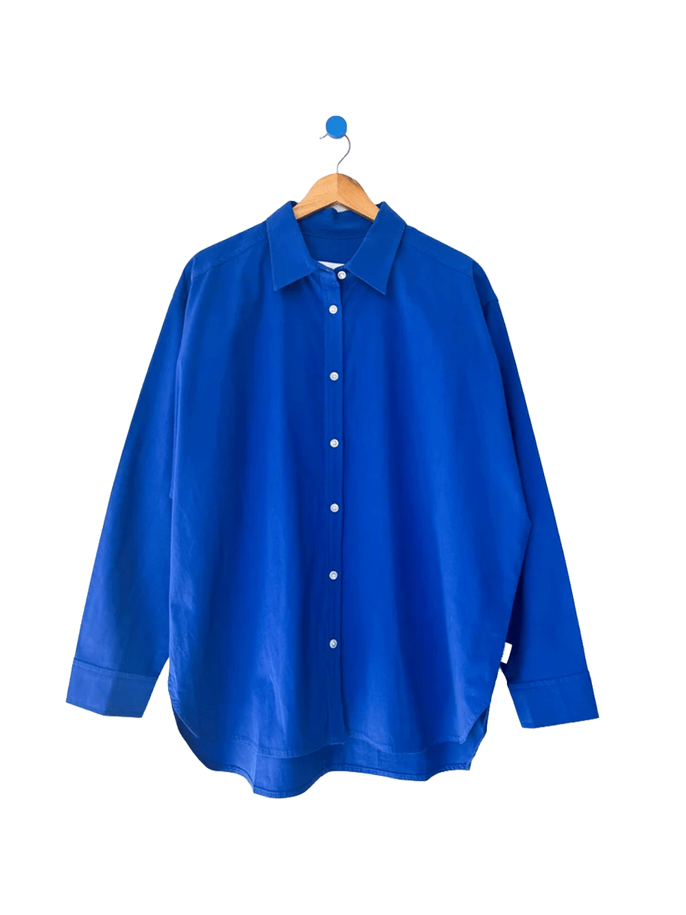 Le Bon Shoppe Owen Shirt in Cobalt hanging on a wooden hanger, featuring a vibrant blue colour, pointed collar, white buttons and relaxed long sleeves | Twentyseven Toronto