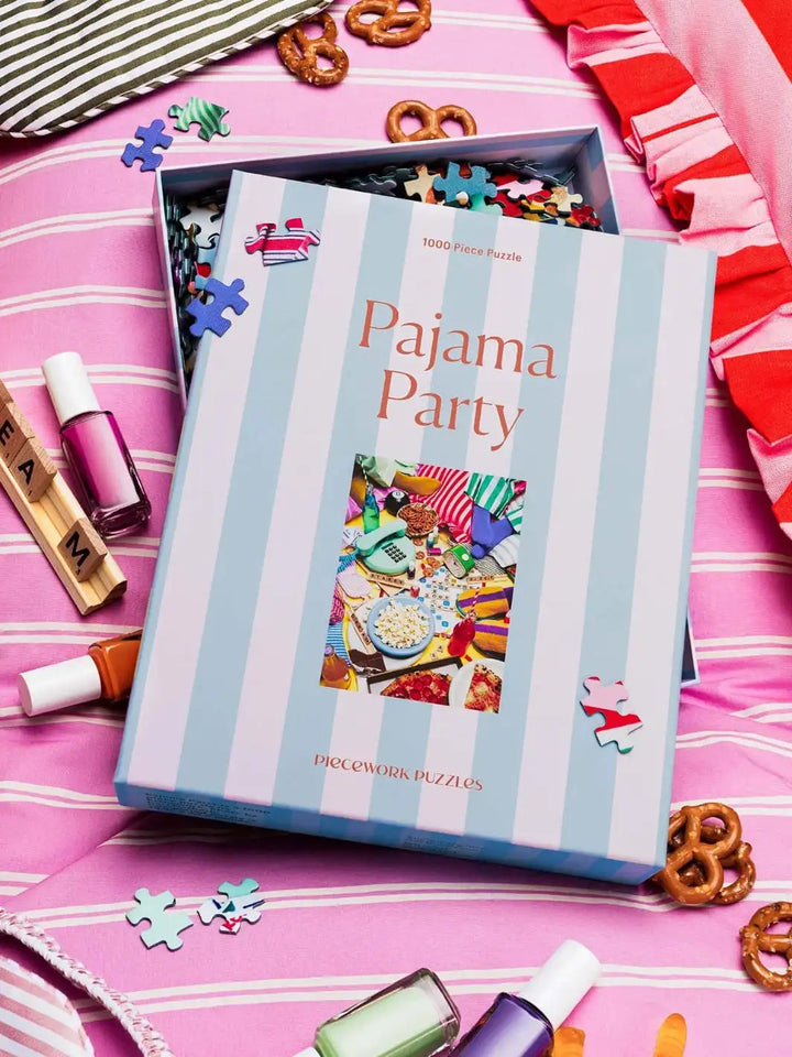 A box of Piecework Puzzles box 'Pajama Party' 1000 piece puzzle on a pink surface with decorative items around | Twentyseven Toronto