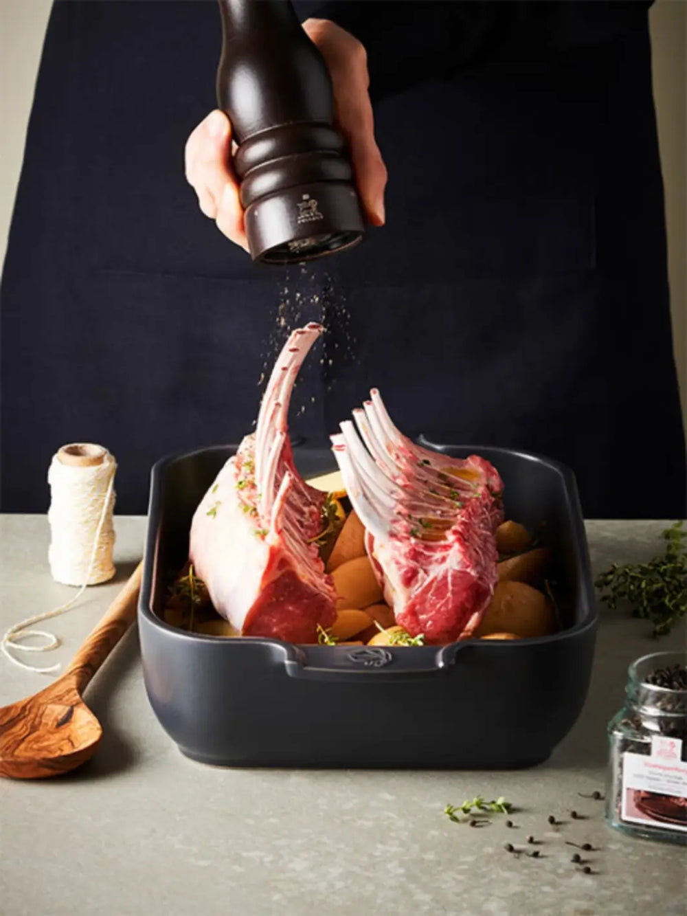 Person seasoning raw lamb chops with Peugeot Paris U Select Wood pepper grinder in a roasting pan on a table | Twentyseven Toronto