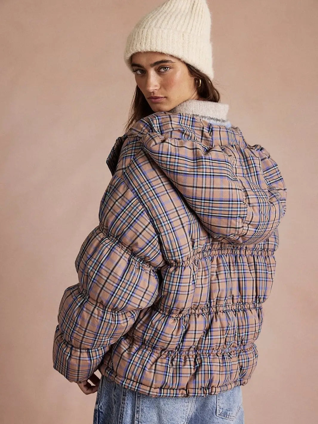 A rear three-quarter view shows a model wearing the hooded Free People Party Of One Puffer Jacket - Tan Combo with a white knit beanie | Twentyseven Toronto