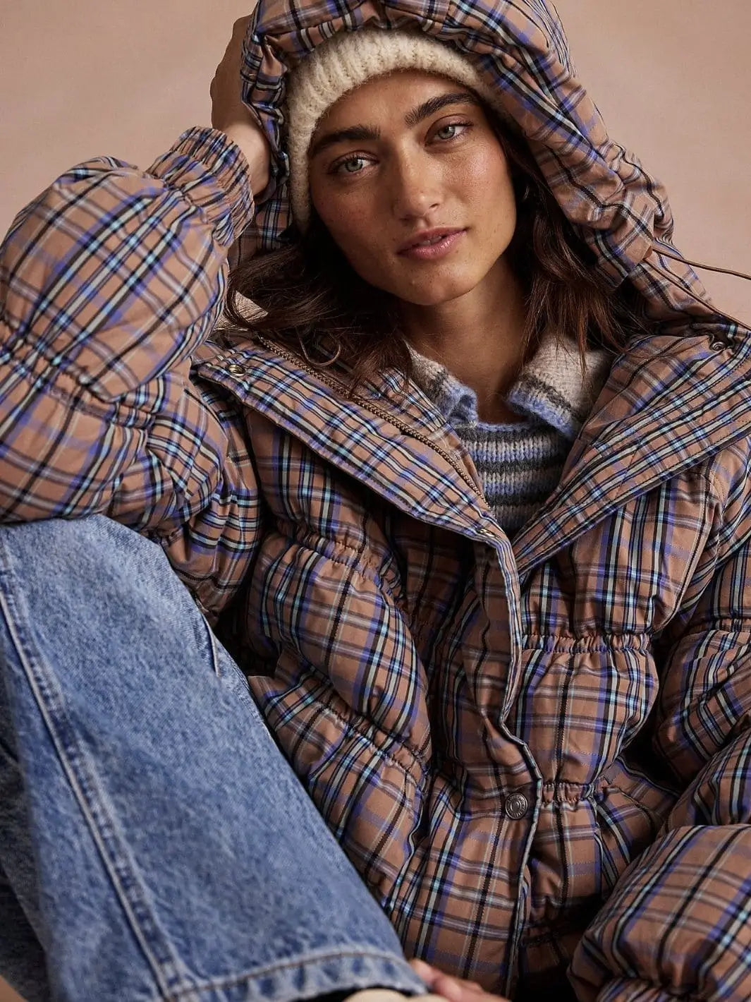 A model adjusts the hood while wearing the cozy, insulated Free People Party Of One Puffer Jacket - Tan Combo layered over a striped sweater | Twentyseven Toronto