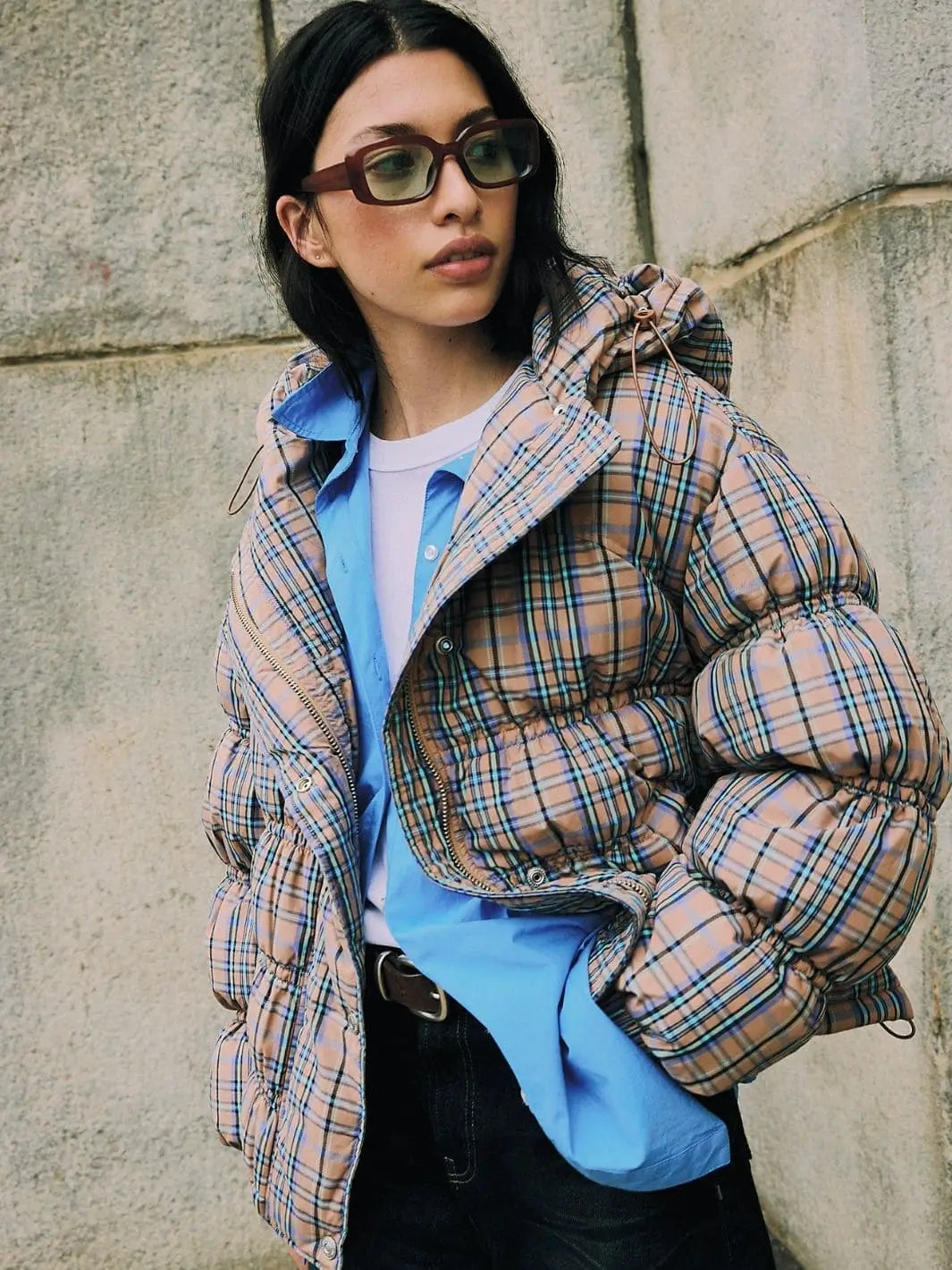 An outdoor shot features a model wearing the open Free People Party Of One Puffer Jacket - Tan Combo styled with a bright blue button-down shirt and sunglasses | Twentyseven Toronto