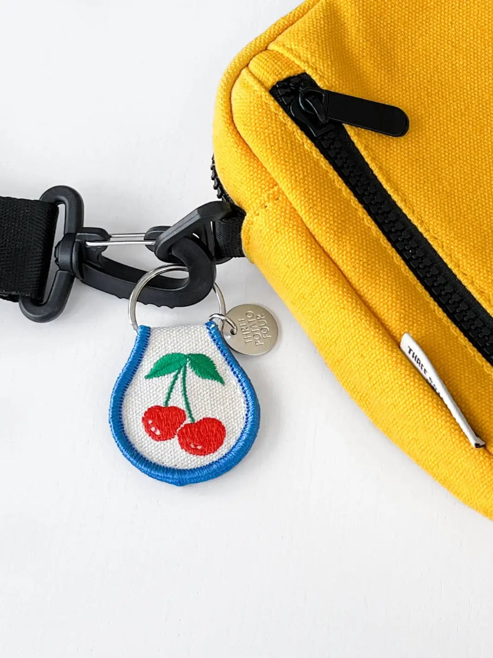 Patch keychain with embroidered cherries design from Three Potato Four attached to a yellow bag on white background | Twentyseven Toronto