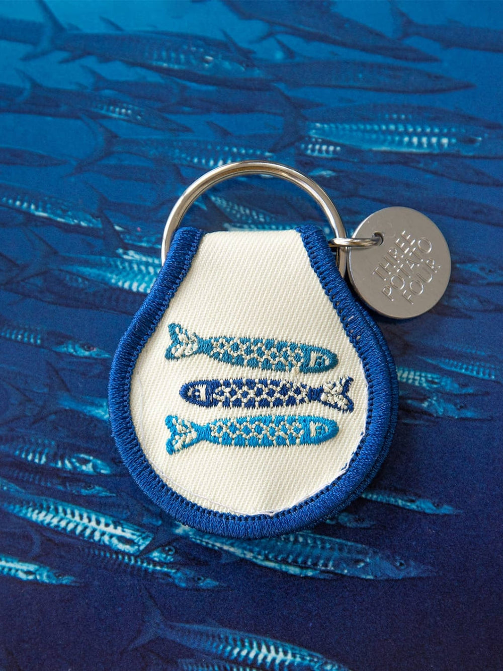 Patch keychain with embroidered fish design from Three Potato Four against blue fish background | Twentyseven Toronto