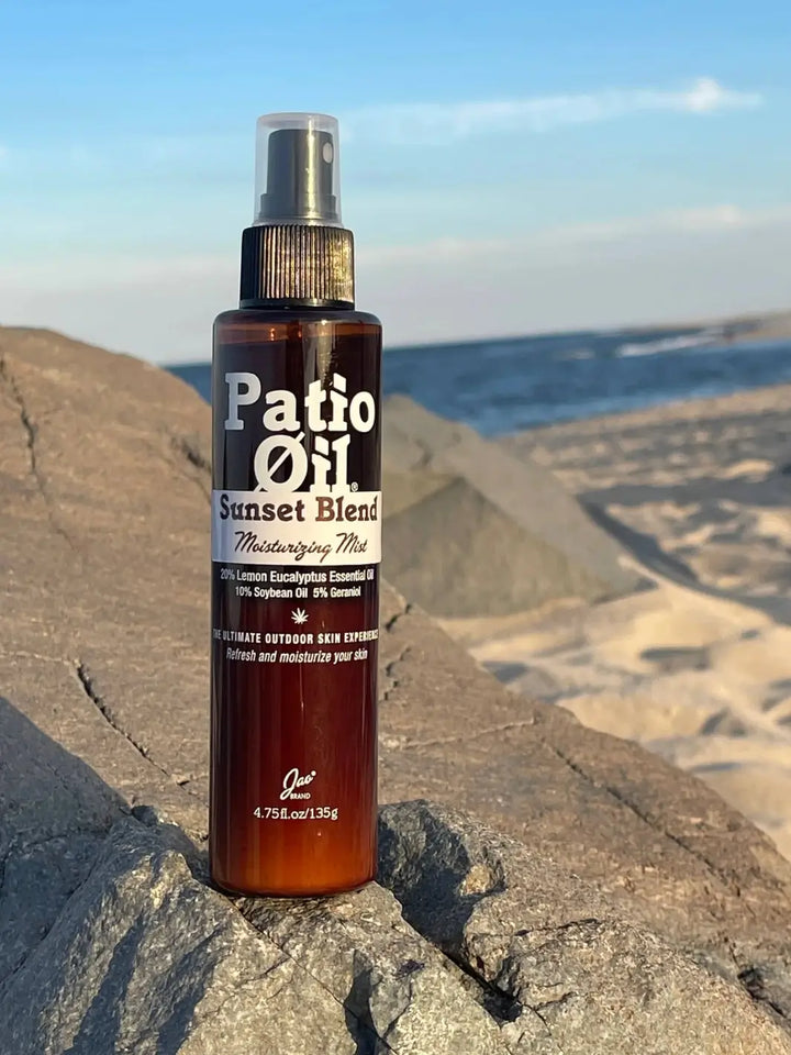 A bottle of Jao Brand Patio Oil Moisturizing Mist sits on a large rock on a sunny beach, with the sand and ocean waves blurred in the background | Twentyseven Toronto