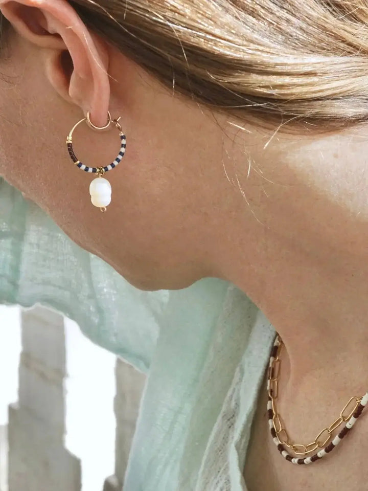 A side profile view shows a person wearing beaded gold hoop earrings adorned with a dangling white freshwater pearl, showcasing the Pearl Drop Hoops from Alice Rise Jewelry | Twentyseven Toronto