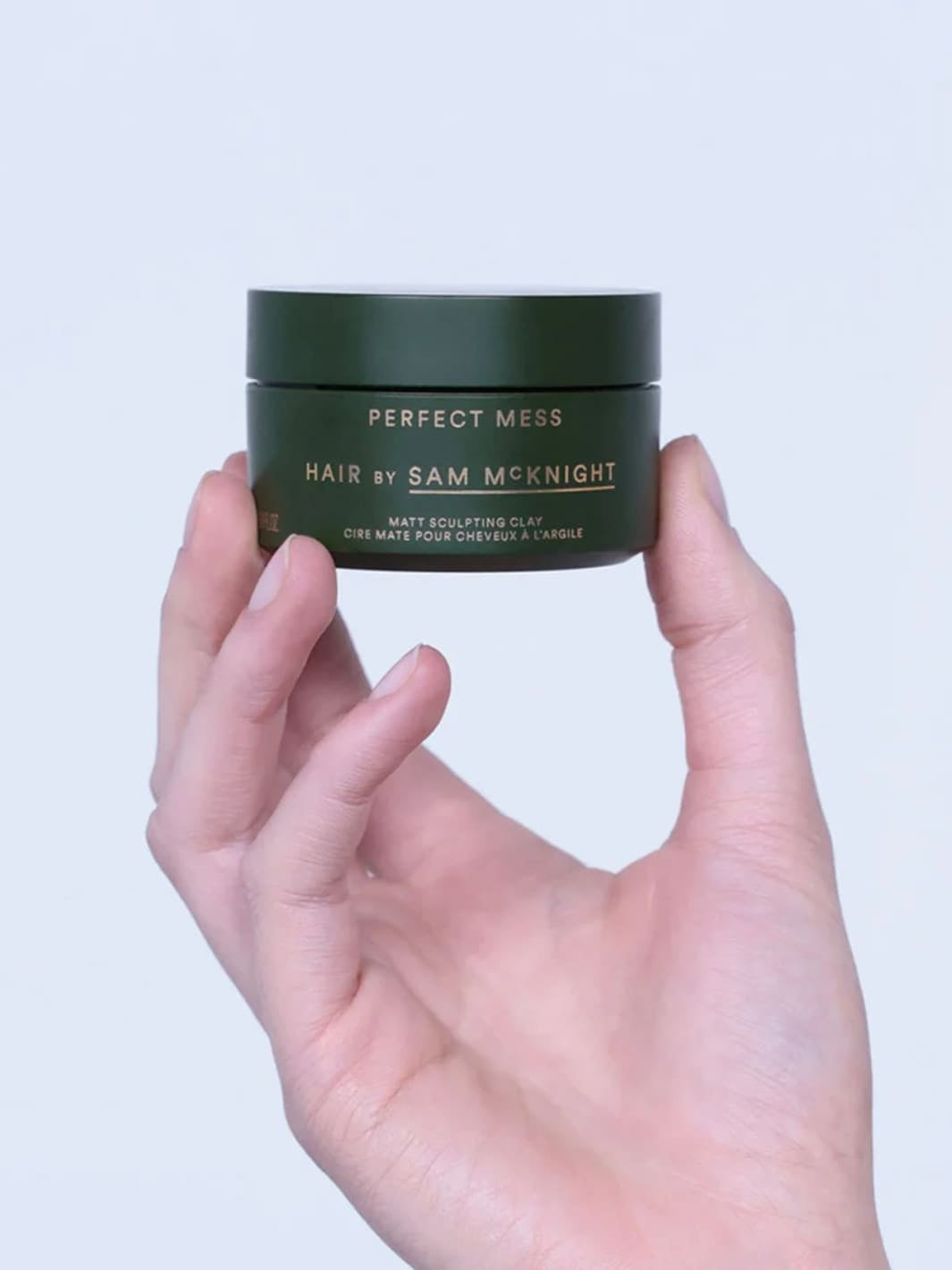 Hand holding a green jar of 'Perfect Mess' Soft Matt Styling Clay by Sam McKnight hair product against a white background, 50ml | Twentyseven Toronto