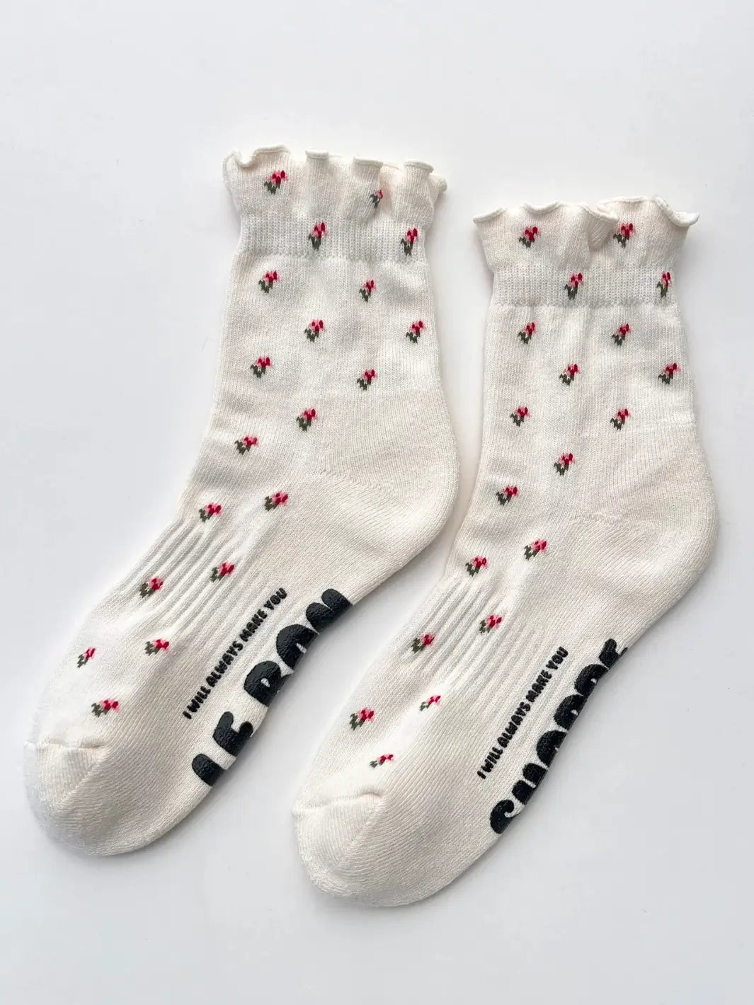 A pair of cream crew socks featuring a small red floral print and ruffled cuffs from the Le Bon Shoppe Petal Ruffled Hugger Crew Socks in Cream Petal set is laid flat on a white surface | Twentyseven