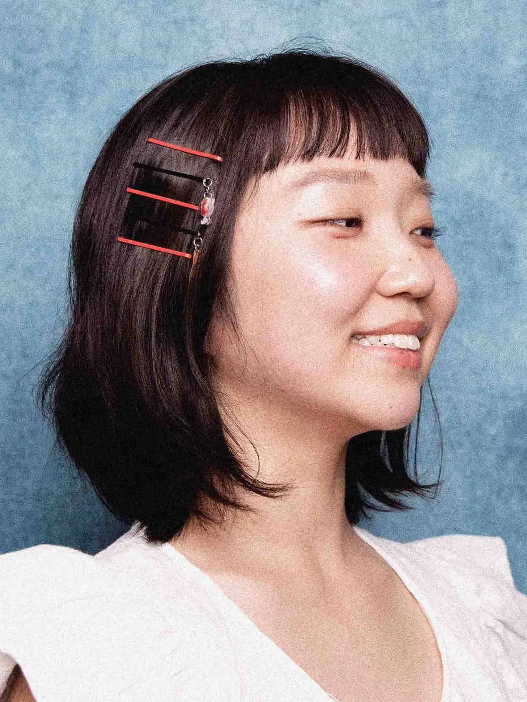 A smiling person with dark hair and bangs wears a row of four red and black Chunks Hairclips Picnic Bobby Pins pinned neatly on the side of their head | Twentyseven Toronto