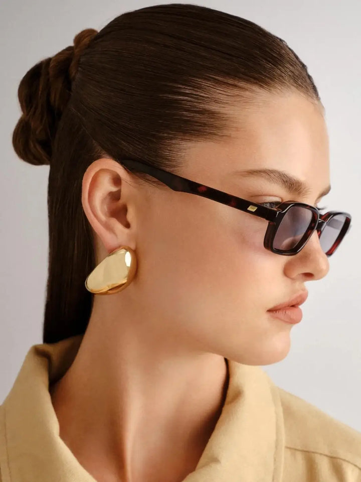 A side profile portrait of a woman showcasing the dark tortoiseshell pattern and temple design of the Le Specs Pilferer - Cherry Tort sunglasses | Twentyseven Toronto