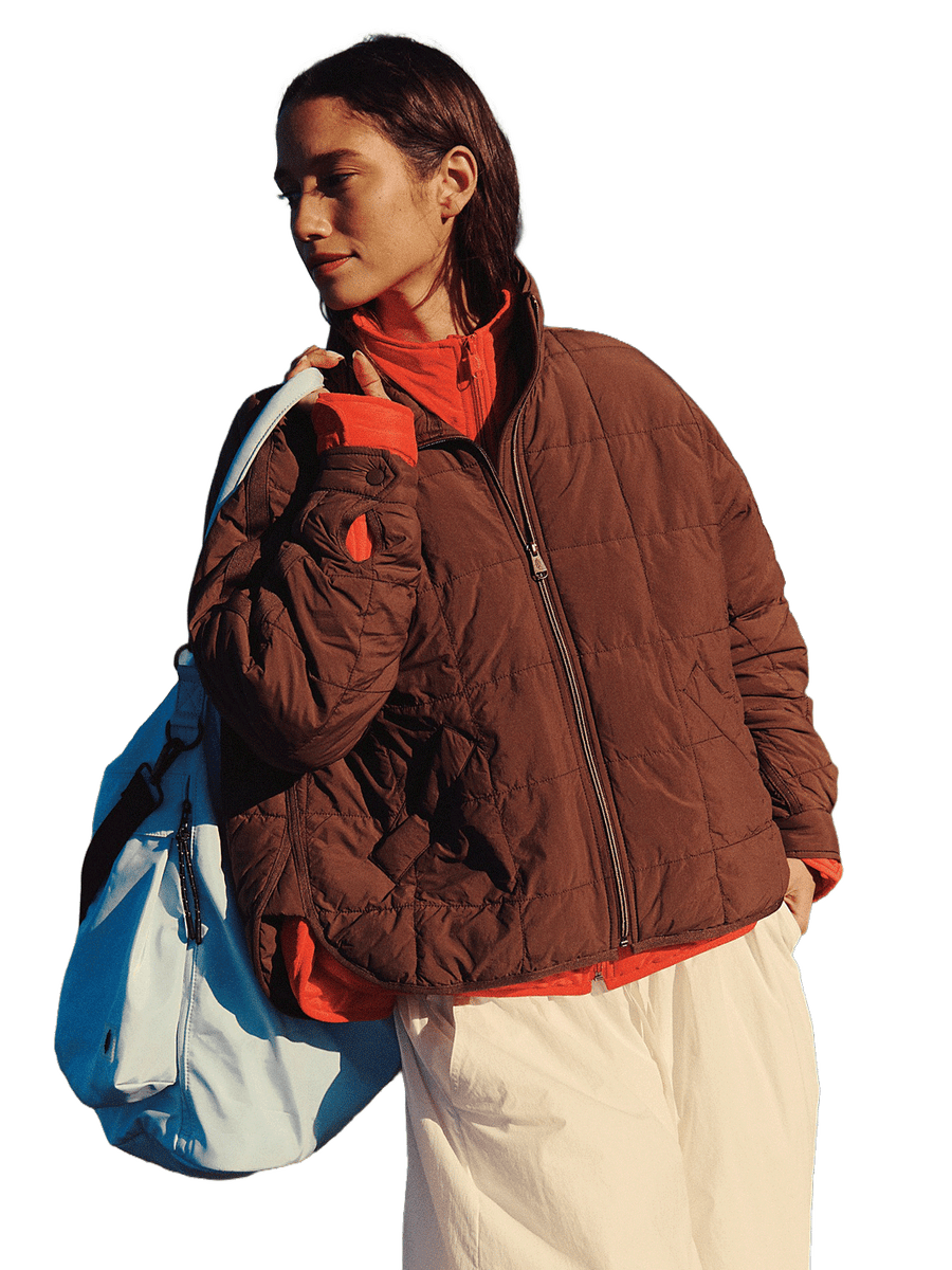 Free People Movement Pippa Packable Puffer in Cocoa styled over a red zip-up with white pants and a blue duffle bag | Twentyseven Toronto