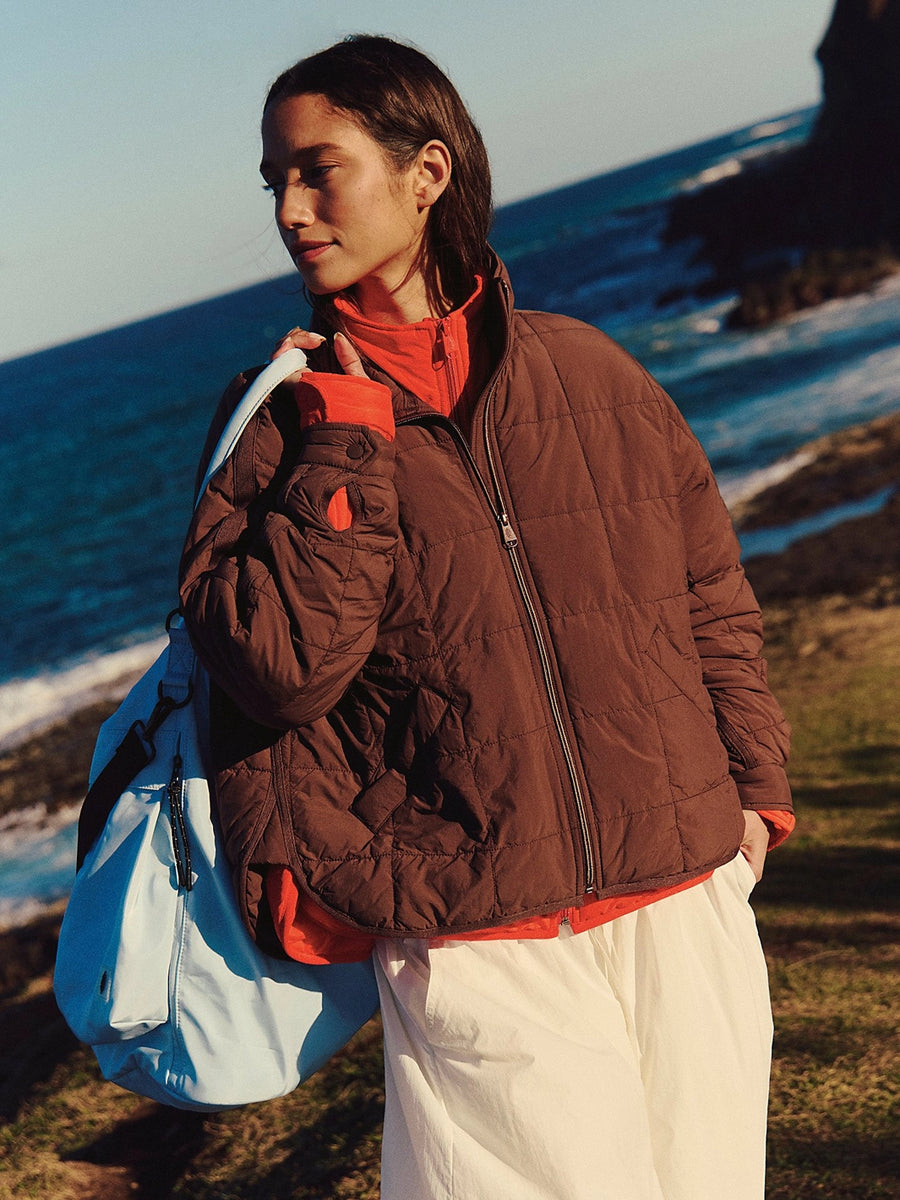 Free People Movement Pippa Packable Puffer in Cocoa styled over a red zip-up with white pants and a blue duffle bag | Twentyseven Toronto
