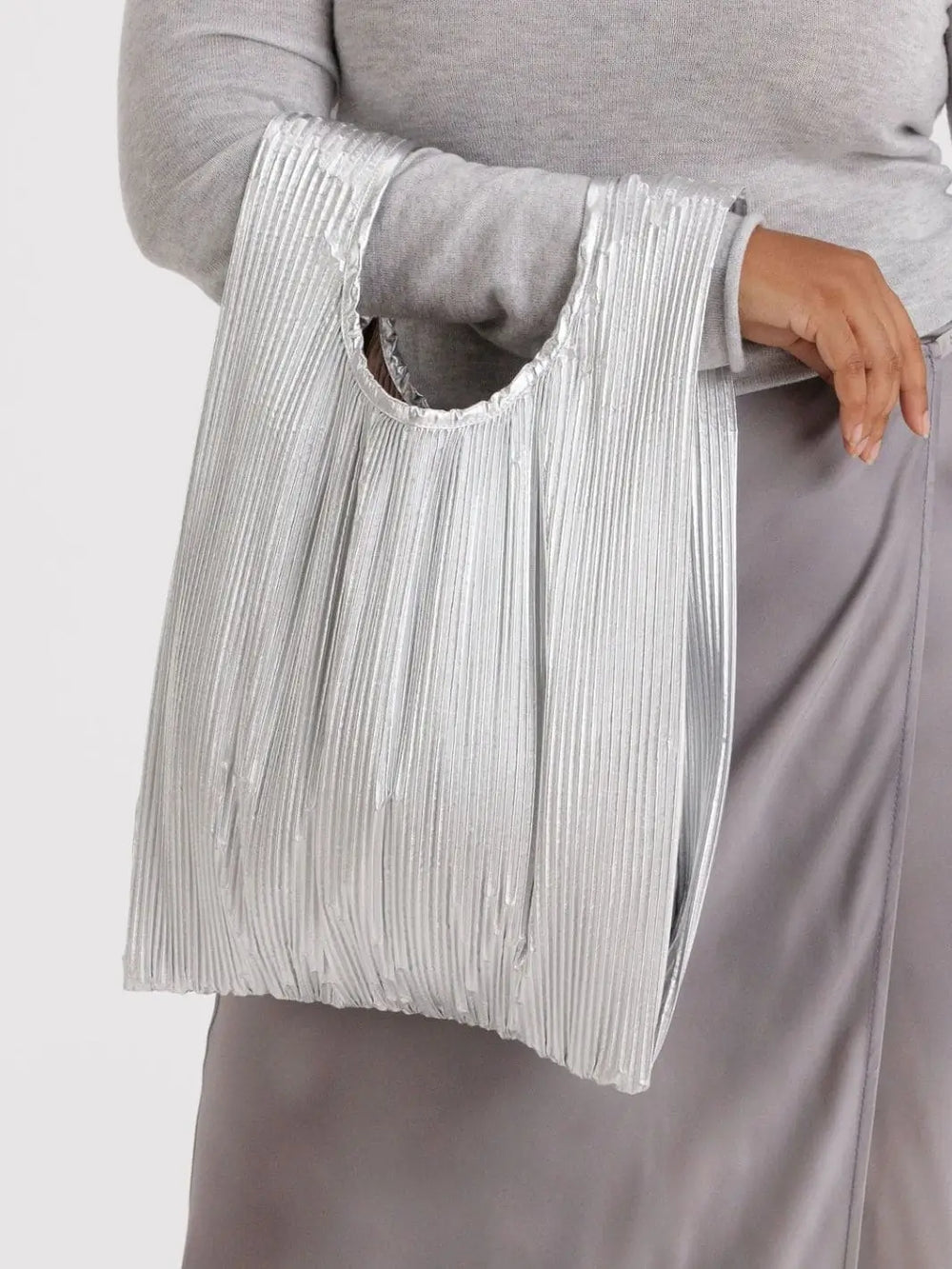 A close-up view of a person wearing a grey top and satin skirt, carrying the unfolded Baggu Pleated Baggu - Chrome Metallic over their arm | Twentyseven Toronto