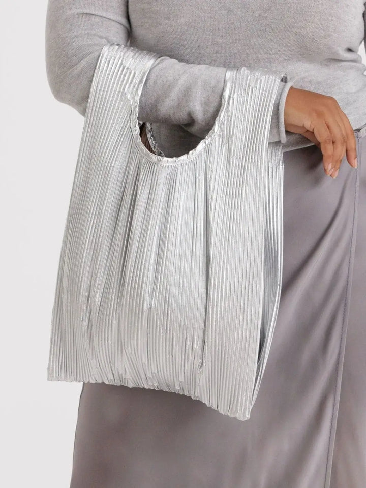 A close-up view of a person wearing a grey top and satin skirt, carrying the unfolded Baggu Pleated Baggu - Chrome Metallic over their arm | Twentyseven Toronto