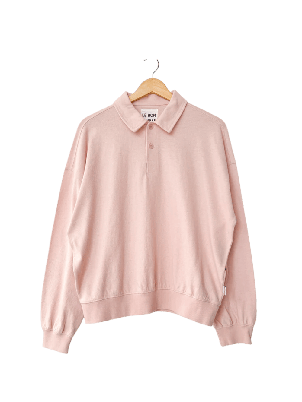 An oversized, light pink Le Bon Shoppe Polo Sweatshirt in Baby Pink with ribbed cuffs hangs from a wooden hanger | Twentyseven Toronto