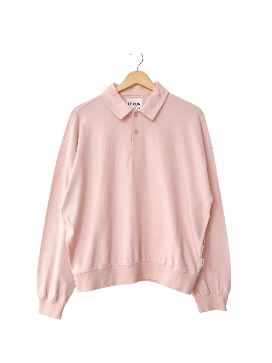 An oversized, light pink Le Bon Shoppe Polo Sweatshirt in Baby Pink with ribbed cuffs hangs from a wooden hanger | Twentyseven Toronto