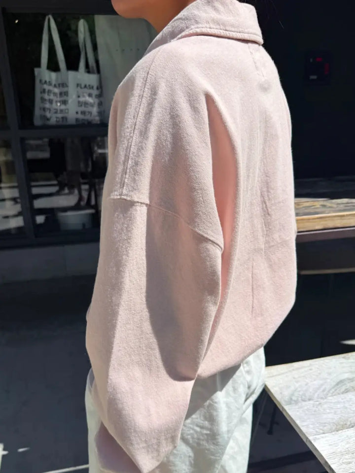 A side view captures a person wearing a relaxed-fit, light pink long-sleeved Le Bon Shoppe Polo Sweatshirt in Baby Pink next to an outdoor table | Twentyseven Toronto