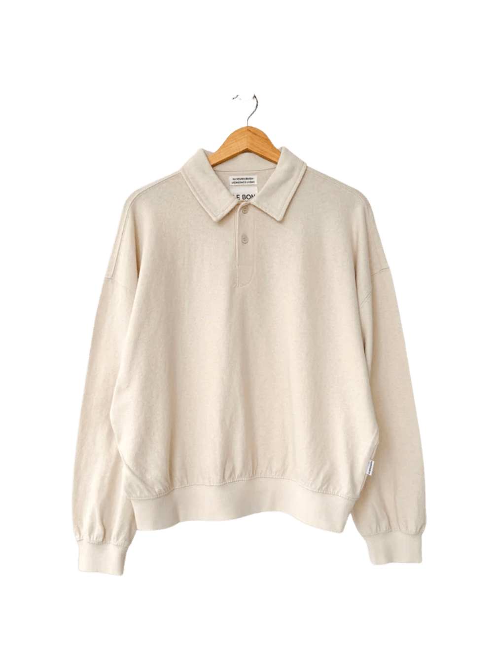 An oversized, long-sleeved Le Bon Shoppe Polo Sweatshirt in Naturel features a buttoned collar and ribbed cuffs while hanging on a wooden hanger | Twentyseven Toronto