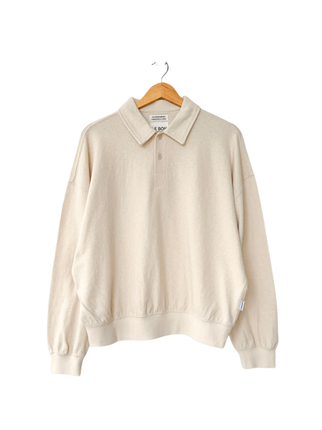 An oversized, long-sleeved Le Bon Shoppe Polo Sweatshirt in Naturel features a buttoned collar and ribbed cuffs while hanging on a wooden hanger | Twentyseven Toronto