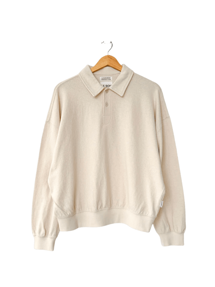 An oversized, long-sleeved Le Bon Shoppe Polo Sweatshirt in Naturel features a buttoned collar and ribbed cuffs while hanging on a wooden hanger | Twentyseven Toronto