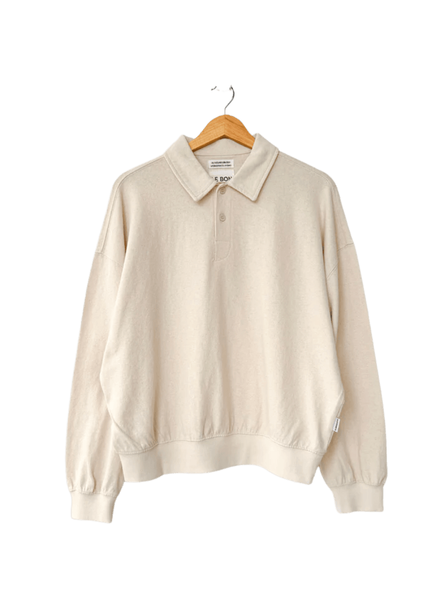 An oversized, long-sleeved Le Bon Shoppe Polo Sweatshirt in Naturel features a buttoned collar and ribbed cuffs while hanging on a wooden hanger | Twentyseven Toronto