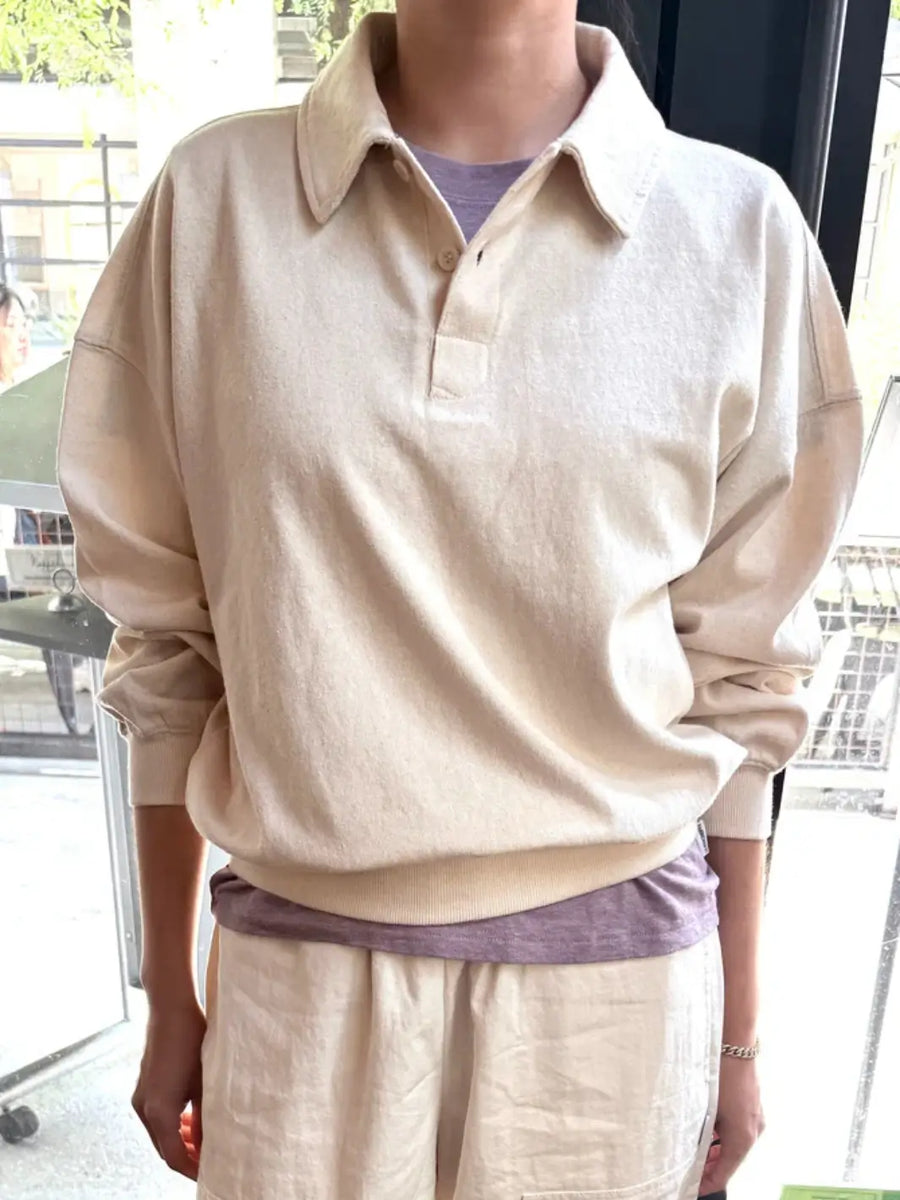 A person wears a textured, off-white Le Bon Shoppe Polo Sweatshirt in Naturel layered over a purple shirt and paired with cream linen pants | Twentyseven Toronto