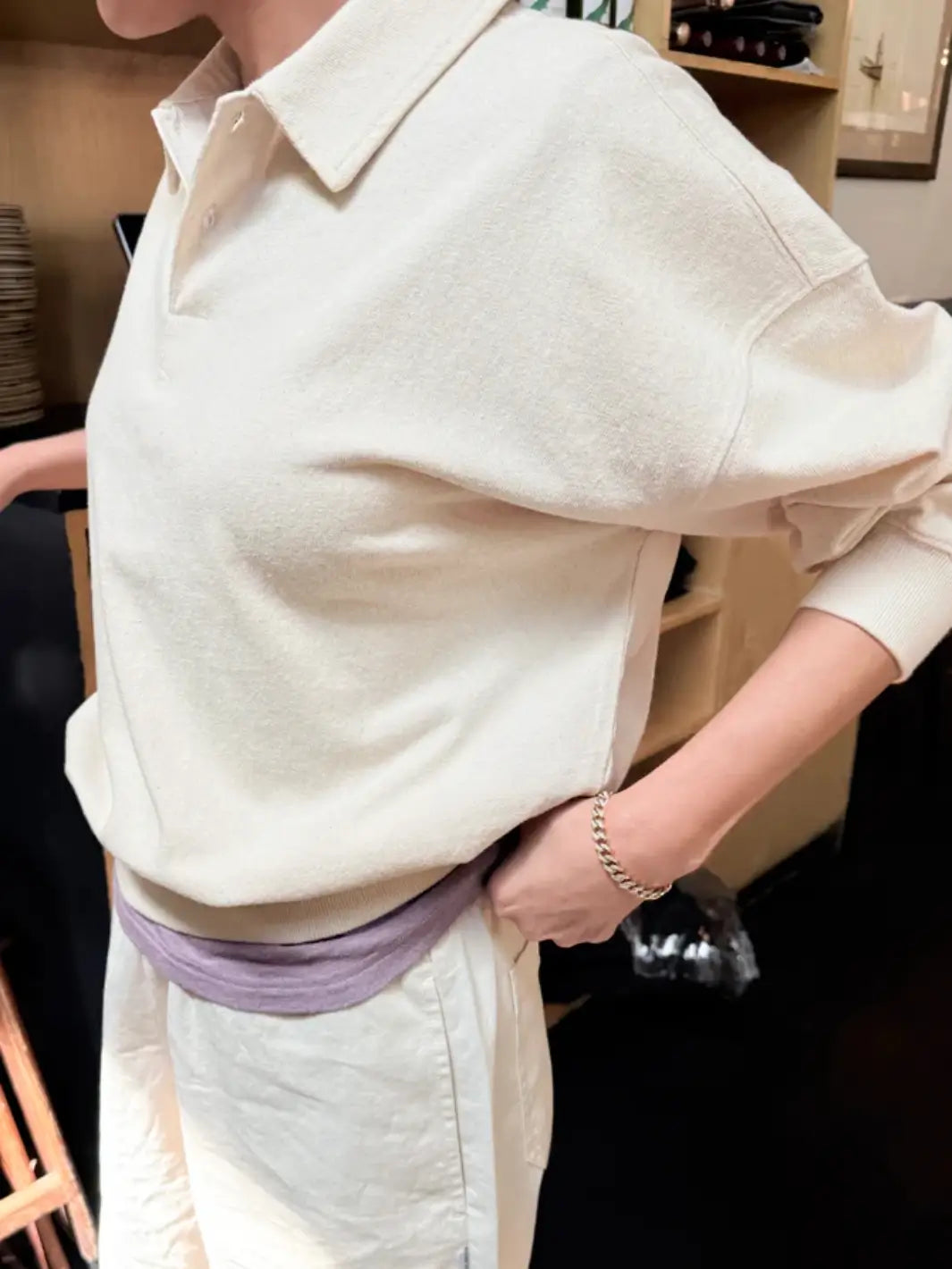 A side view shows a person wearing a loose-fitting Le Bon Shoppe Polo Sweatshirt in Naturel with their hand tucked into the pocket of cream trousers | Twentyseven Toronto