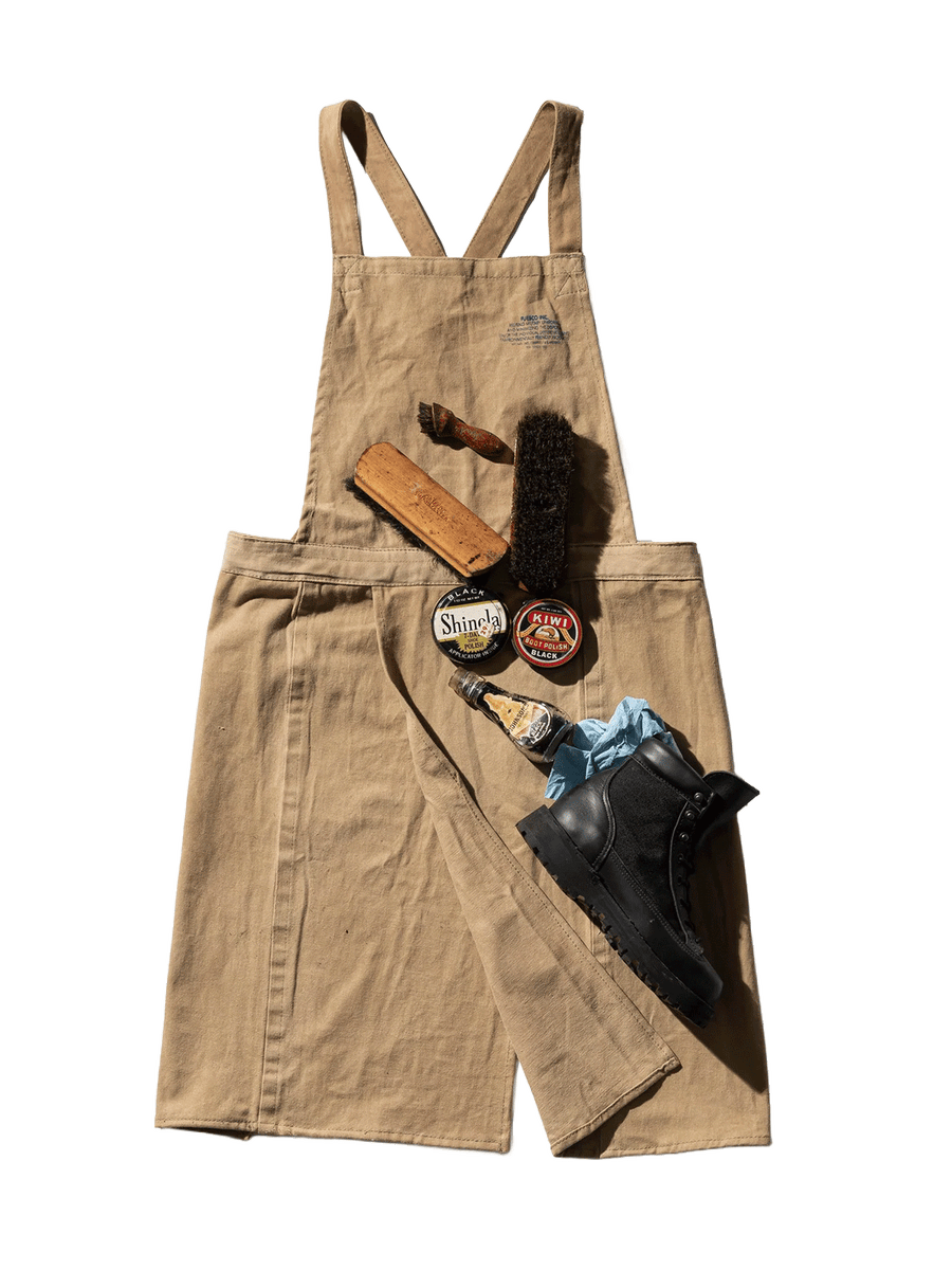 Puebco Potters Apron in beige repurposed fabric, styled with shoe brushes, black shoe polish tins and a black leather boot to showcase its practical design | Twentyseven Toronto
