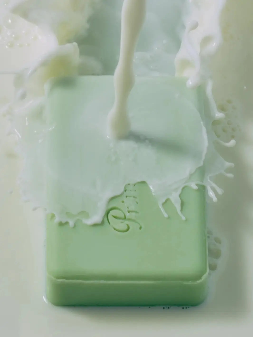 Action shot of creamy white liquid pouring directly onto the green Flamingo Estate Prinsesstarta Milk Bar soap, creating a splash effect | Twentyseven