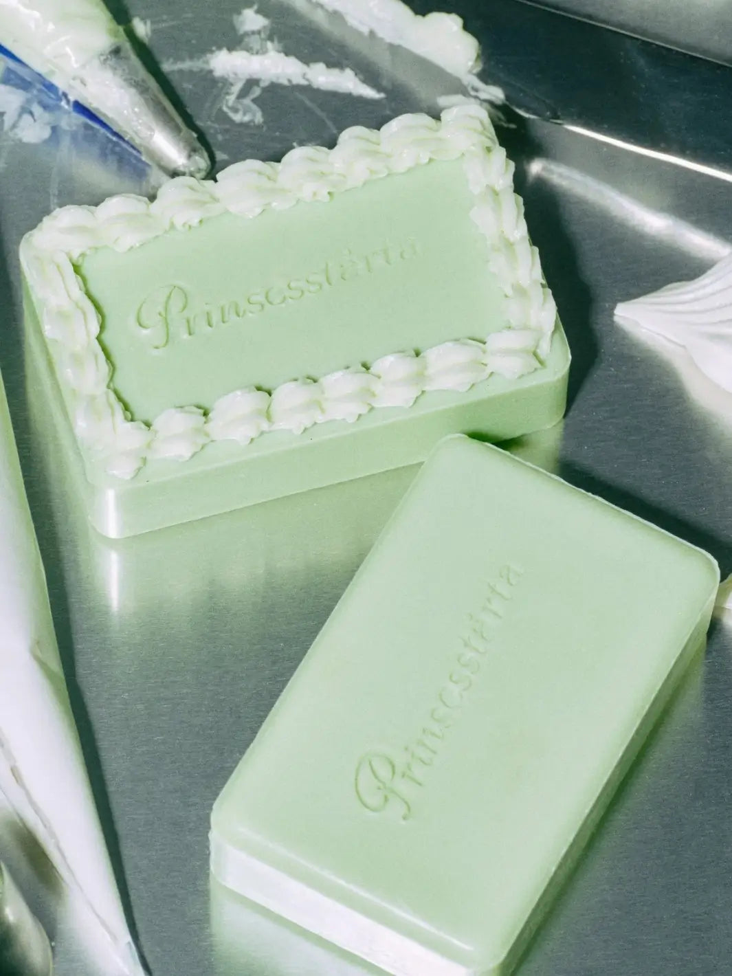 High-angle shot showing a plain green bar of Flamingo Estate Prinsesstarta Milk Bar next to a matching soap decorated with white piped frosting borders | Twentyseven