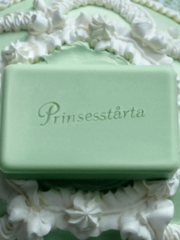 Close-up of the green Flamingo Estate Prinsesstarta Milk Bar soap bar resting on a cake surface surrounded by ruffled white frosting | Twentyseven