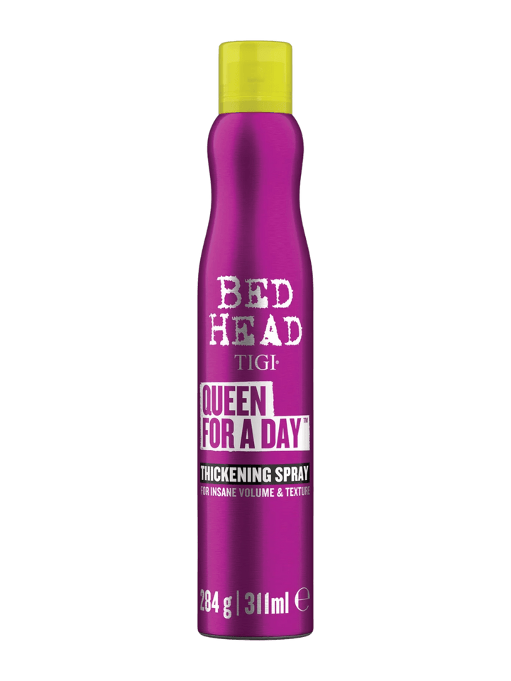 A hand wearing a gold link bracelet holds up a metallic purple bottle of Bedhead by TIGI Queen for a Day Thickening Spray | Twentyseven Toronto