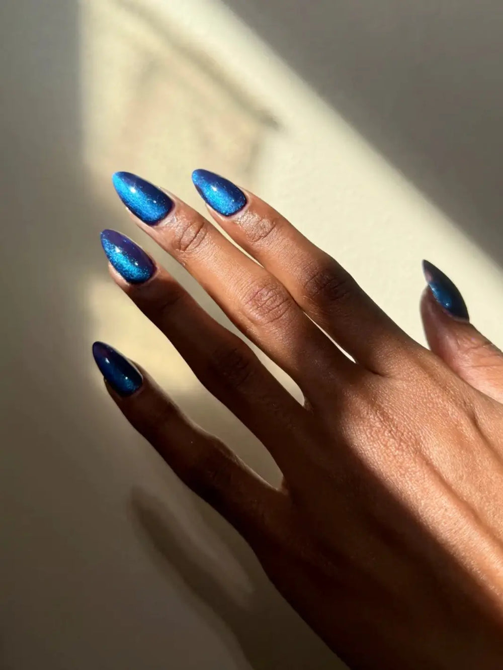 A hand with long, almond-shaped nails features the shimmering deep blue and purple hues of Death Valley Nails Quietude (Or Swallowing Certain Unhappiness) Magnetic Nail Polish under sunlight | Twentyseven Toronto