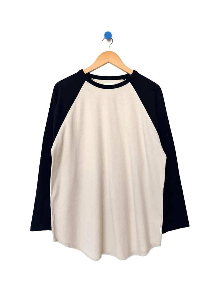 Heavy Cotton Raglan Tee in Naturel/Black on a wooden hanger, featuring a cream body, contrasting black long raglan sleeves, ribbed crew neckline and curved hem | Twentyseven Toronto