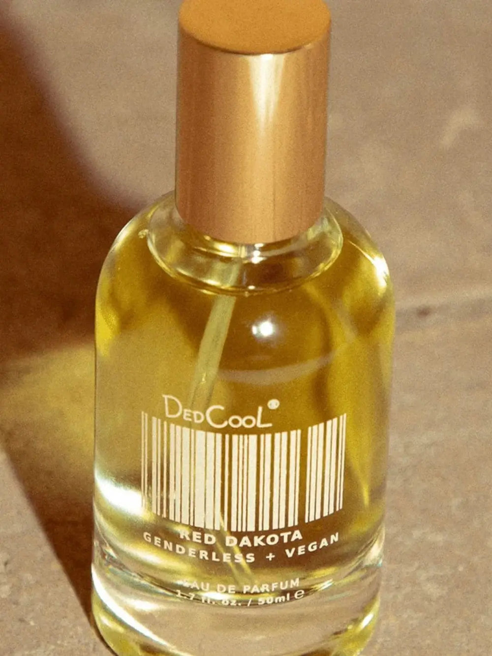 A 50ml glass bottle of Dedcool Red Dakota Fragrance filled with golden liquid is shown in close-up under warm lighting | Twentyseven Toronto
