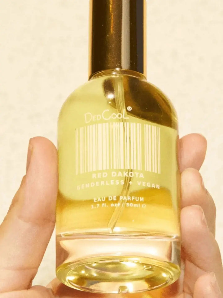 A hand cradles a full-sized bottle of Dedcool Red Dakota Fragrance, showcasing the white barcode label and clear product text | Twentyseven Toronto