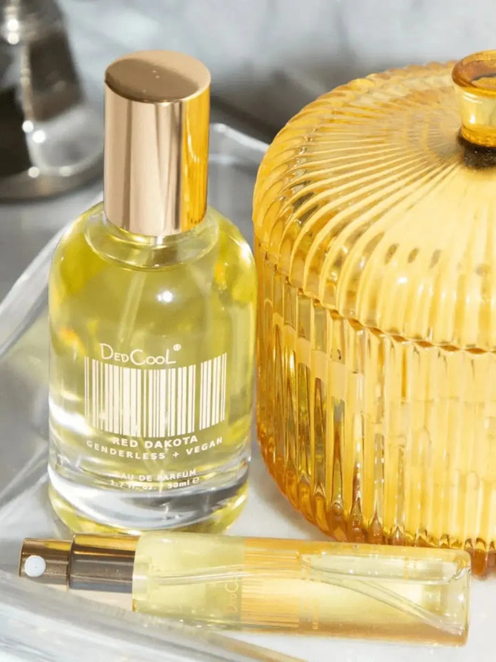 A 50ml bottle and a 15ml travel spray of Dedcool Red Dakota Fragrance rest on a silver tray next to a ribbed, amber glass jar | Twentyseven Toronto