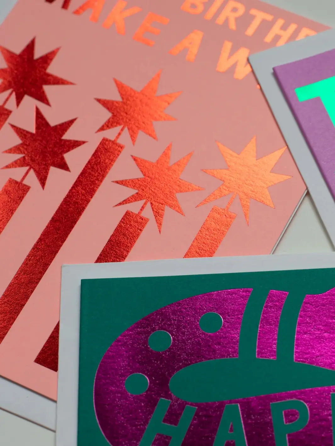 An extreme close-up highlights the shiny, reflective texture of the metallic candles on the Banquet Workshop Red Foil Happy Birthday Make a Wish Note Card alongside other foil-stamped cards | Twentyseven
