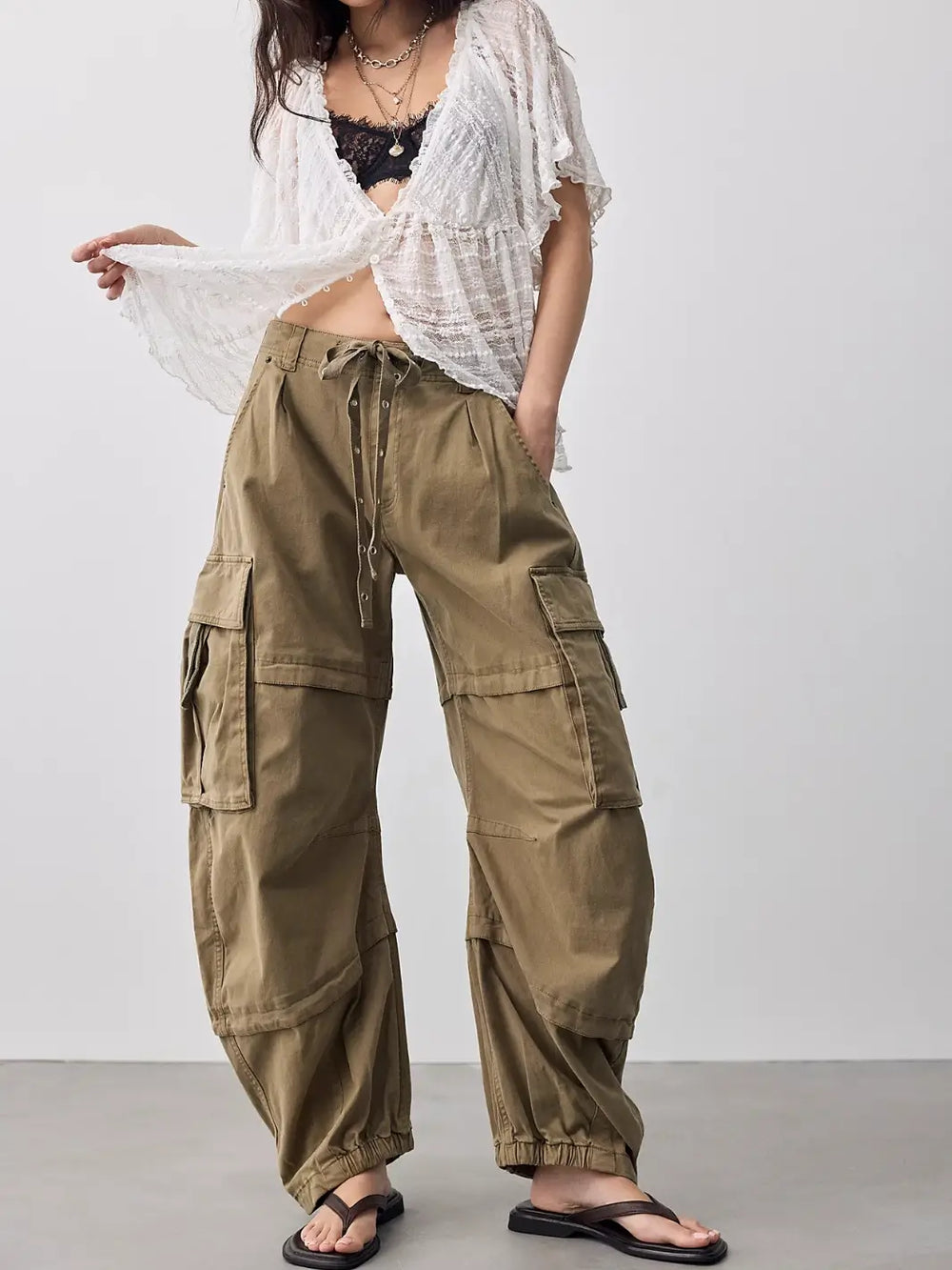 Front view of a model wearing Free People We the Free Reef Curved Twill Cargo Pants in Aloe styled with a white lace blouse and sandals | Twentyseven