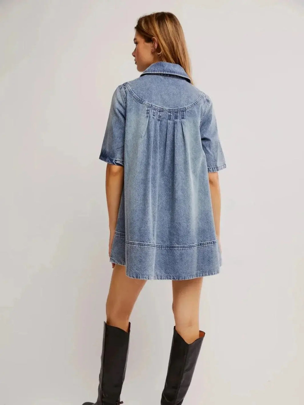 A rear view highlights the curved yoke, pleated back detail, and relaxed A-line shape of the Free People Remino Denim Mini - Ocean Blue paired with black tall boots | Twentyseven Toronto