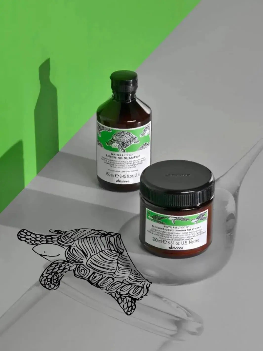 A bottle of Davines RENEWING Shampoo and a tub of conditioning treatment stand on a grey surface featuring a black-and-white turtle illustration against a bright green backdrop | Twentyseven Toronto