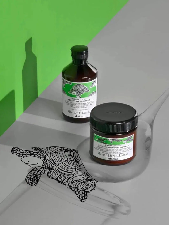 A bottle of Davines RENEWING Shampoo and a tub of conditioning treatment stand on a grey surface featuring a black-and-white turtle illustration against a bright green backdrop | Twentyseven Toronto