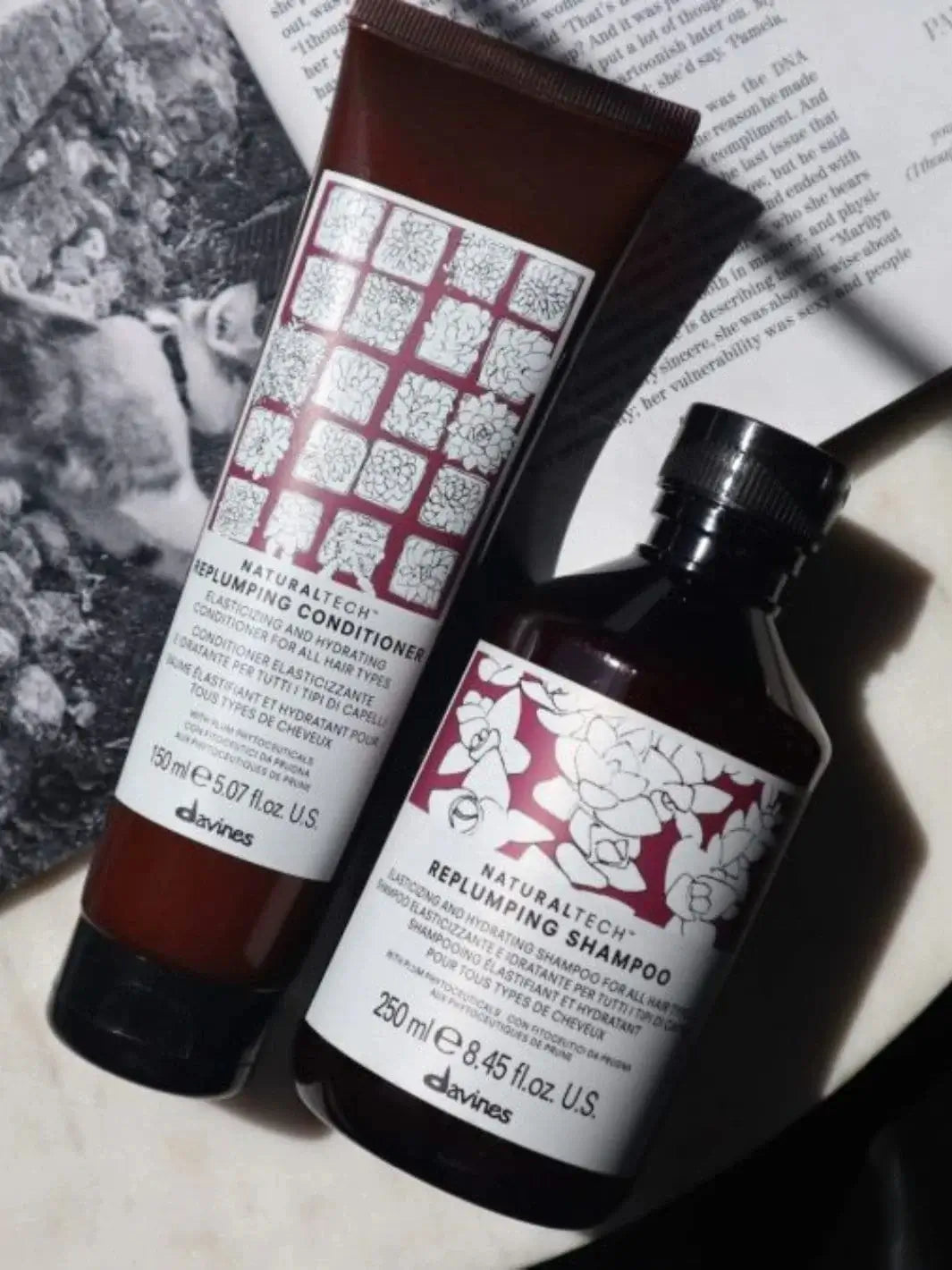 A tube of Davines REPLUMPING Conditioner lies next to a matching bottle of shampoo on top of a magazine | Twentyseven Toronto