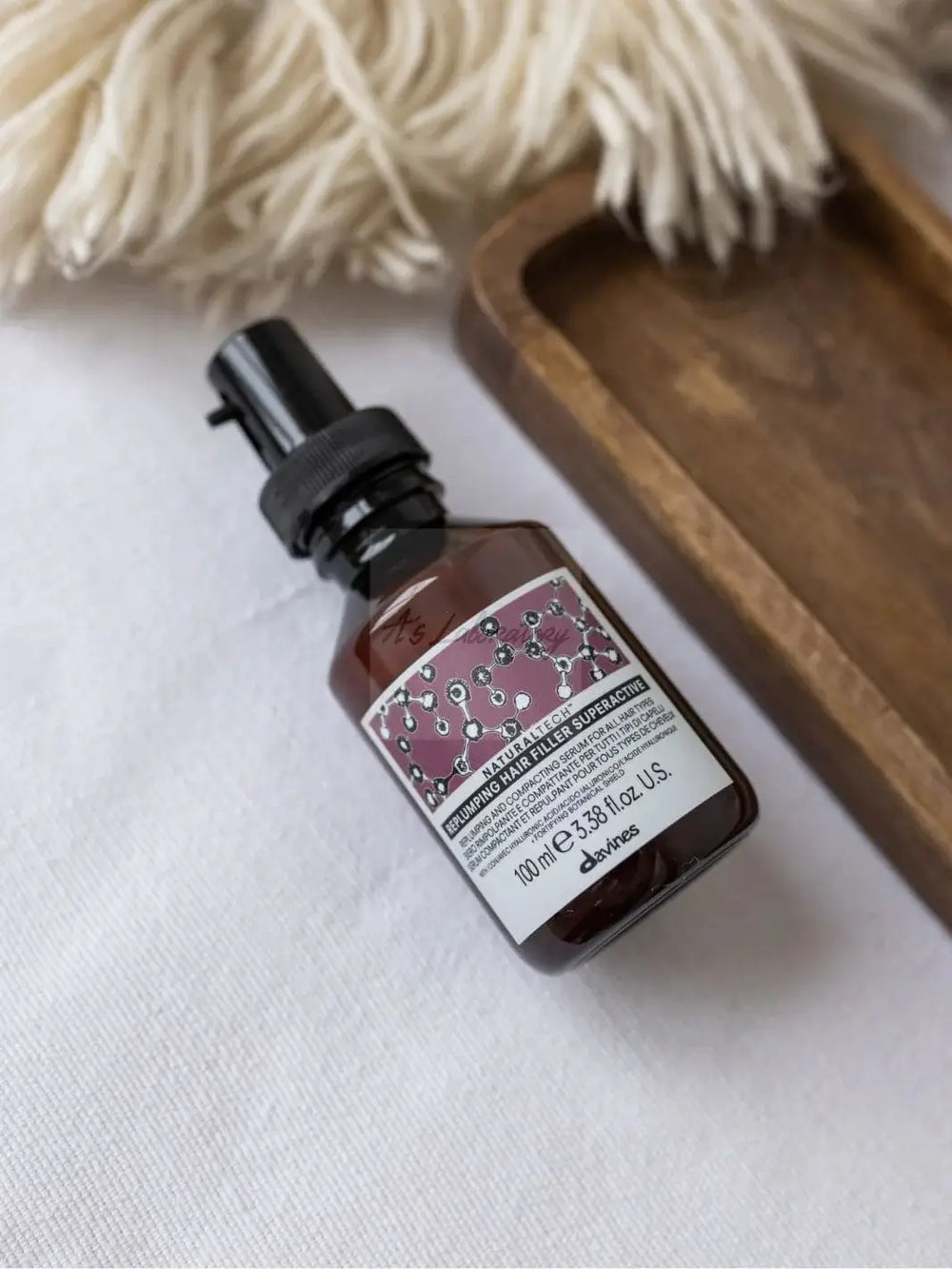 An amber spray bottle of Davines REPLUMPING Hair Filler Superactive rests on a white textured surface next to a small wooden tray | Twentyseven Toronto