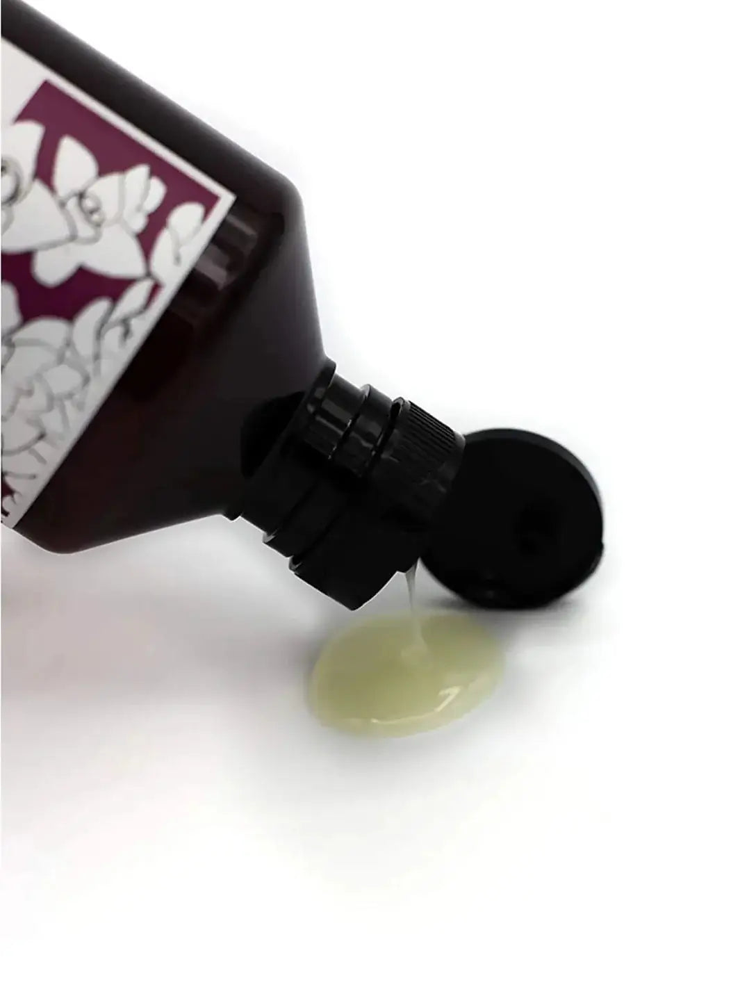 A clear, light green liquid pours out from the open cap of a Davines REPLUMPING Shampoo bottle onto a white surface | Twentyseven Toronto
